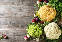 Variety of fresh raw organic colorful cauliflower, cabbage romanesco and radish with bundle of coriander