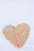A heart shape made with colorful sprinkles on a white surface
