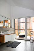 Modern bathroom with high ceiling and glass wall leading to balcony