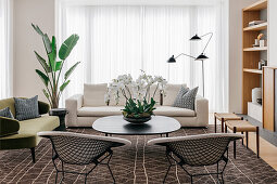 Retro seating and coffee table on brown patterned carpet in front of patio door with floor-length curtain