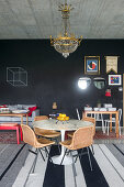 Runder Tisch mit Rattanstühlen unter Kronleuchter, im Hintergrund schwarze Tafelwand
