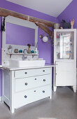 Sink on old chest of drawers and corner cabinet in purple bathroom