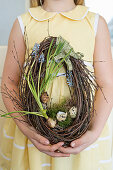 Girl holding egg-shaped Easter wreath with grape hyacinths and quail eggs