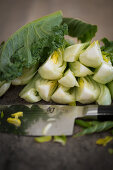 Bok choy cut into quarters, with a knife on a wooden chopping board