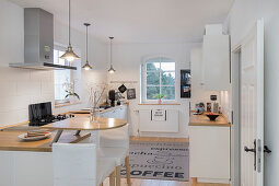 weiße Küche mit halbrunder Frühstückstheke an Küchenzeile und Barhockern in umgebauter Molkerei