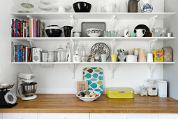 Crockery and kitchen utensils on three shelves above worksurface