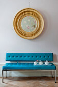 Round gilt-framed mirror above tea service on bright blue couch