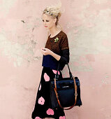 Junge blonde Frau in Pullover, schwarzem Rock mit rosa Herzen, und mit Handtasche und Haarreifen