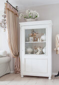 Old pictures and soup tureens in white cabinet with glass door