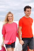 A blonde woman wearing a pink top and a brunette man wearing an orange t-shirt on a beach