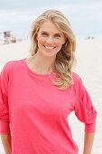 A young blonde woman on a beach wearing a pink top