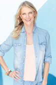 A young blonde woman wearing a denim shirt over a light top