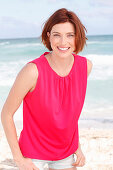 A red-haired woman by the sea wearing a pink top