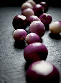 Purple and white pearl onions scattered on a black slate countertop