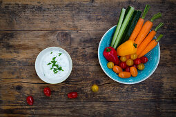 A bowl of carrots, peppers, cucumber, tomatoes and a chive dip