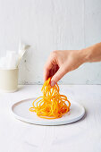 A hand piling carrot noodles on a plate