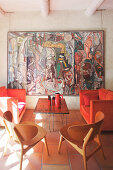 Mediterrane Lounge mit Holzstühlen, roter Sofagarnitur und großformatigem Kunstwerk an der Wand