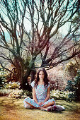 A young woman sitting in a meadow wearing a floral patterned dress