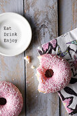 A bitten doughnut with pink frosting on a colourful napkin