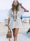 Junge Frau in weißem, kurzem Sommerkleid und mit Halskette am Strand