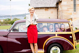 A blonde woman standing by a car full of kids