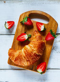 Fresh croissant and ripe berries on vintage rustic chopping board over white wooden background
