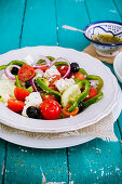 Greek salad in a white bowl on a turquoise table