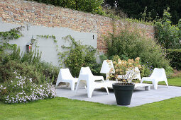 weiße Plastikstühle auf der Terrasse an der Gartenmauer