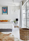 Doppelbett in weißem Schlafzimmer, im Vordergrund Tierfellteppich und Korb