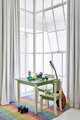 Toys on child's table, chairs and guitar next to window in high-ceilinged room