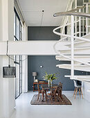 Dining table and chairs next to glass wall in high-ceilinged room with white spiral staircase in foreground