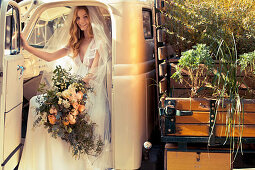 Braut in weißem Hochzeitskleid mit üppigem Brautstrauß sitzt in einem Pickup