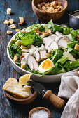 Classic Caesar salad with grilled chicken breast and half of egg in white ceramic plate