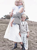 A blonde woman wearing a sleeveless jumper and a white skirt with two children