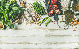 Winter vegetarian, vegan food cooking ingredients, vegetables, fruit, beans, cereals, kitchen utencil, dried flowers, olive oil over white painted wooden background