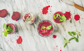Fresh morning beetroot smoothie or juice in glasses with mint leaves over grey marble background, top view
