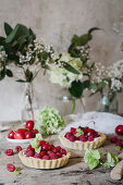 Kirsch-Himbeertorteletts auf Holztisch, im Hintergrund Blumen in Vasen