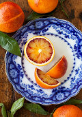A blue and white plate with pieces of blood orange, with whole blood oranges and leaves in the background