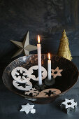 Two lit candles amongst star and snowflake pendants in bowl