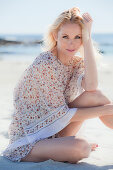 A blonde woman on a beach wearing a patterned tunic