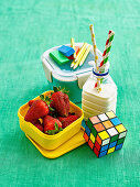 Erdbeeren in Lunchbox, Milchflasche, Stifte und Zauberwürfel