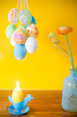 Mit Gouache-Farben bemalte Ostereier, Kerze und Blumenvase