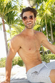 A young, topless man wearing sunglasses and shorts
