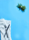 Cutlery, a cloth and a bunch of herbs on a blue surface