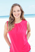 A blonde woman by the sea wearing a pink top