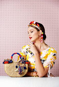 A young woman wearing a head piece made from pompoms with a yellow-patterned summer dress