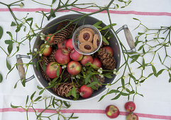 Alter Topf mit Weihnachtsäpfeln, Misteln, Zapfen und Marmeladenplätzchen