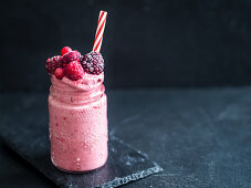 A frozen smoothie with berries in glass with a straw (vegan)