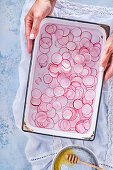 A woman holding a tray of radish slices in water
