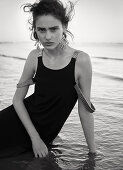 A dark-haired woman wearing a black dress by the sea (black-and-white shot)